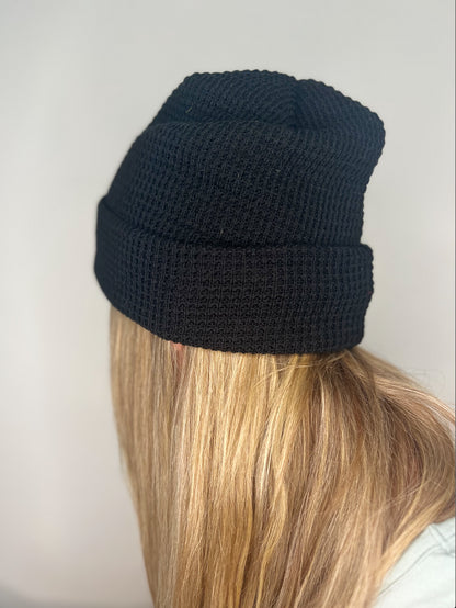 Tuque en tricot gaufré recyclée couleur noire, vue de côté, portée par une femme, mettant en avant les détails du tricot gaufré et la coupe profil moyen.